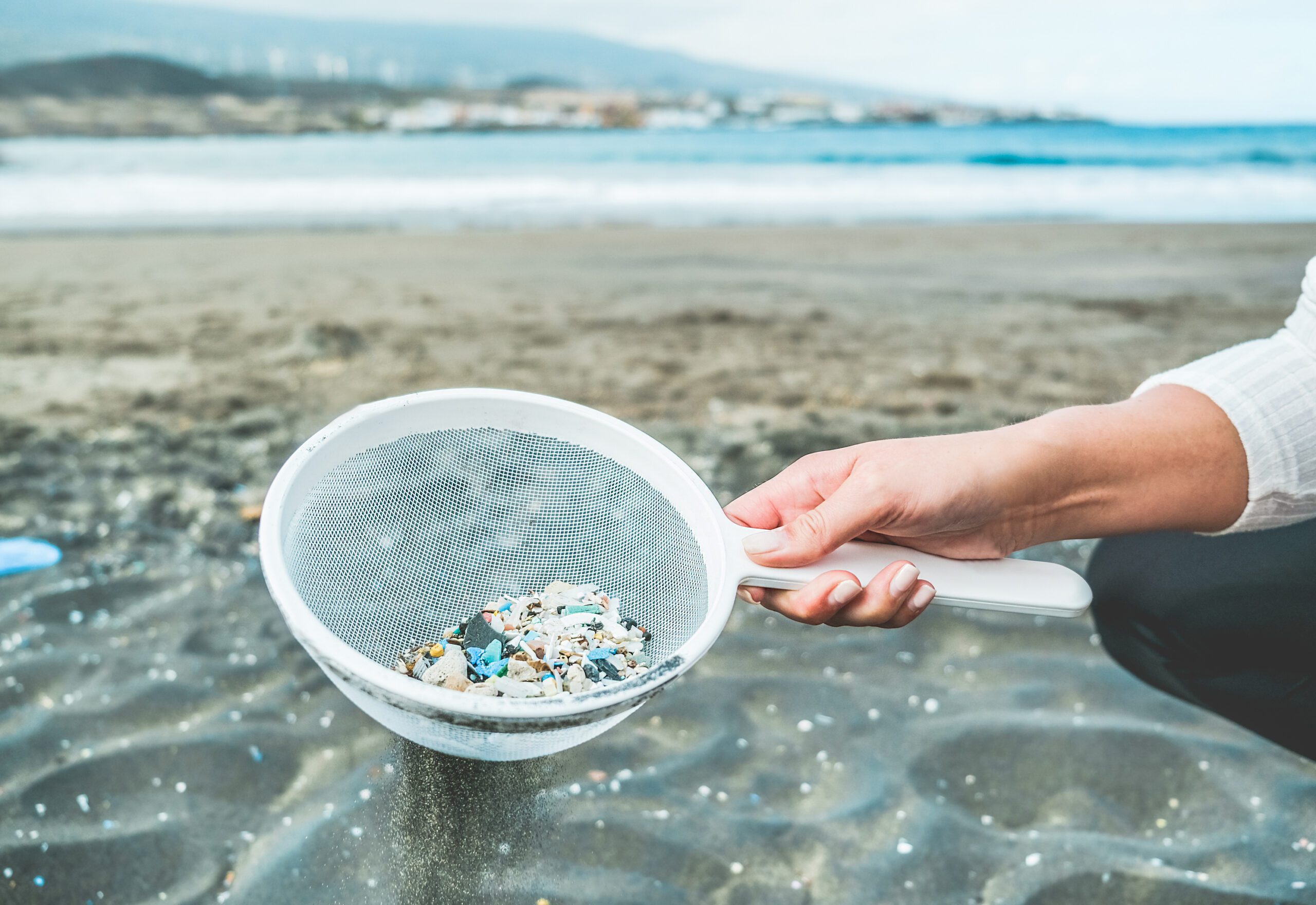 Young woman cleaning microplastics from sand on the beach - Environmental problem, pollution and ecolosystem warning concept - Focus on hand Young woman cleaning microplastics from sand on the beach - Environmental problem, pollution and ecolosystem warning concept - Focus on hand